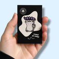 Hand holding a black card with an enamel pin badge featuring a raccoon and 'CHAOS' text.