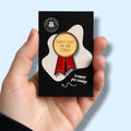Enamel pin badge with 'Didn't Quit My Job Today' text held in a hand against a light blue background